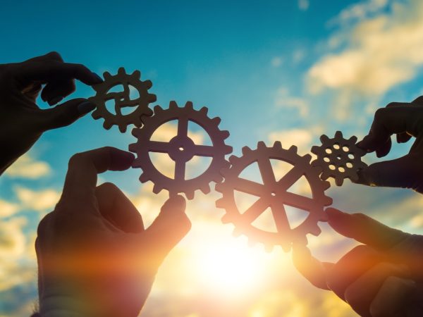 Four hands of businessmen connect gears to a puzzle on a background of sunset. Business concept idea, partnership, cooperation, teamwork, community, creative